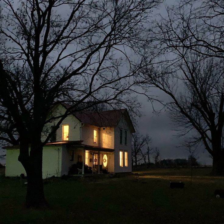 a white house sitting in the middle of a field at night with lights on it's windows