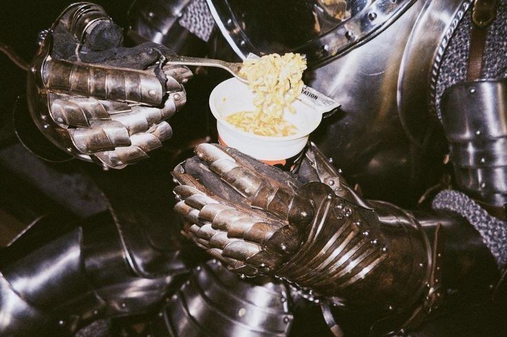 a close up of a person wearing armor eating food from a bowl on their hands