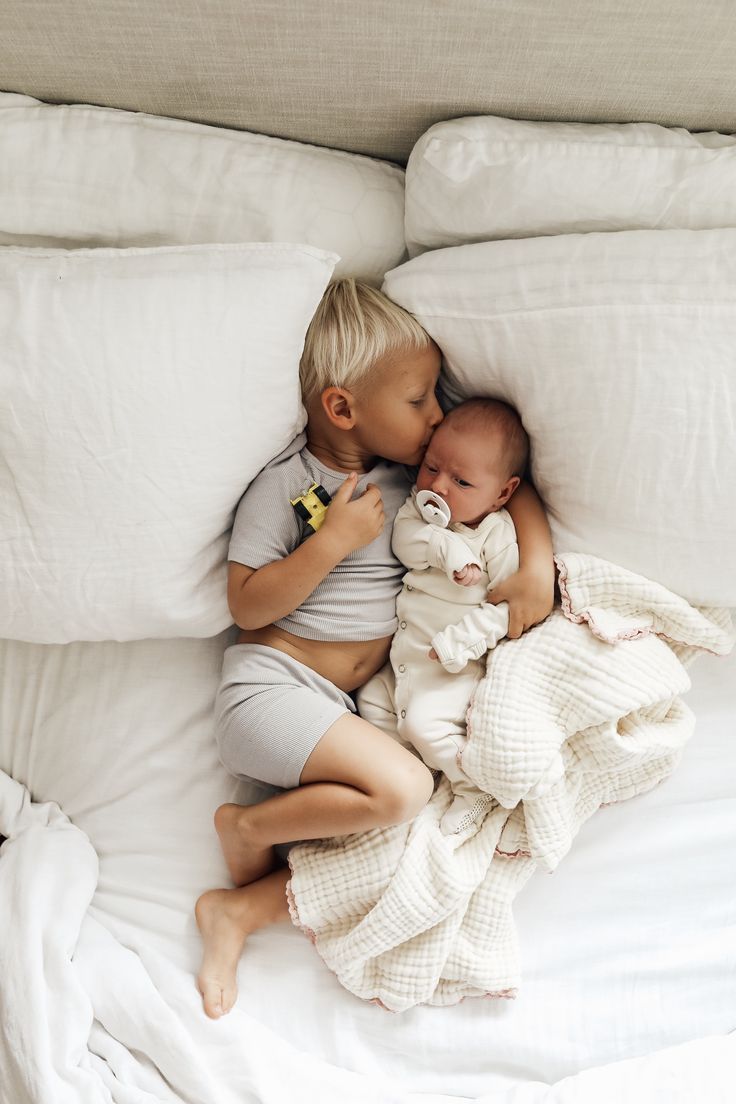 two babies are laying on top of each other in the middle of a white bed