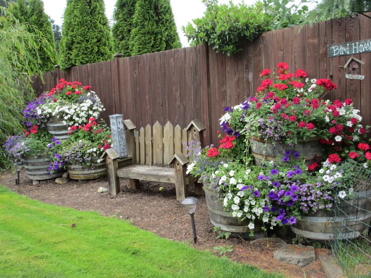 a wooden bench sitting next to a garden filled with potted plants and flowers in front of a fence