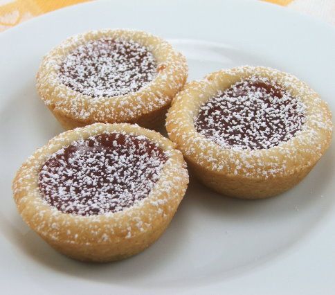 three cookies with powdered sugar on top sit on a white plate next to a yellow table cloth