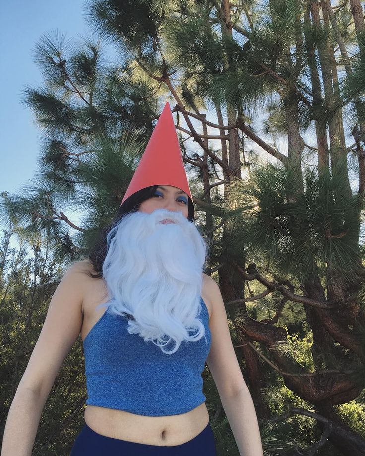 a woman wearing a gnome hat and blue swimsuit standing in front of pine trees