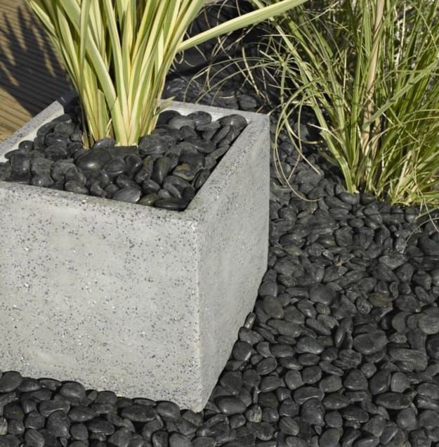 a cement planter filled with lots of rocks and plants next to some grass on the ground