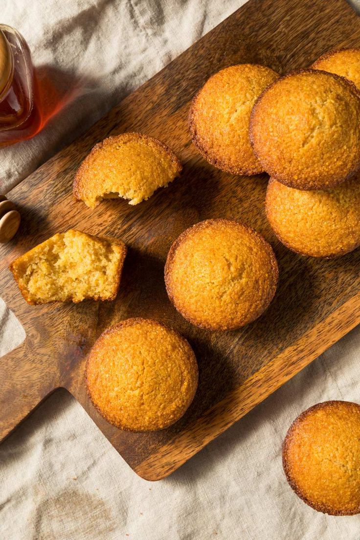 several muffins on a wooden cutting board next to a cup of tea and honey