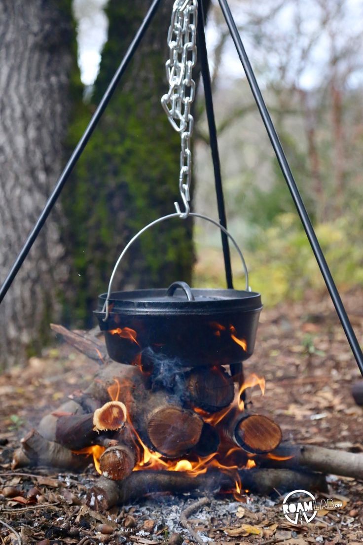 an open fire pit with chains hanging from it's sides in front of a tree