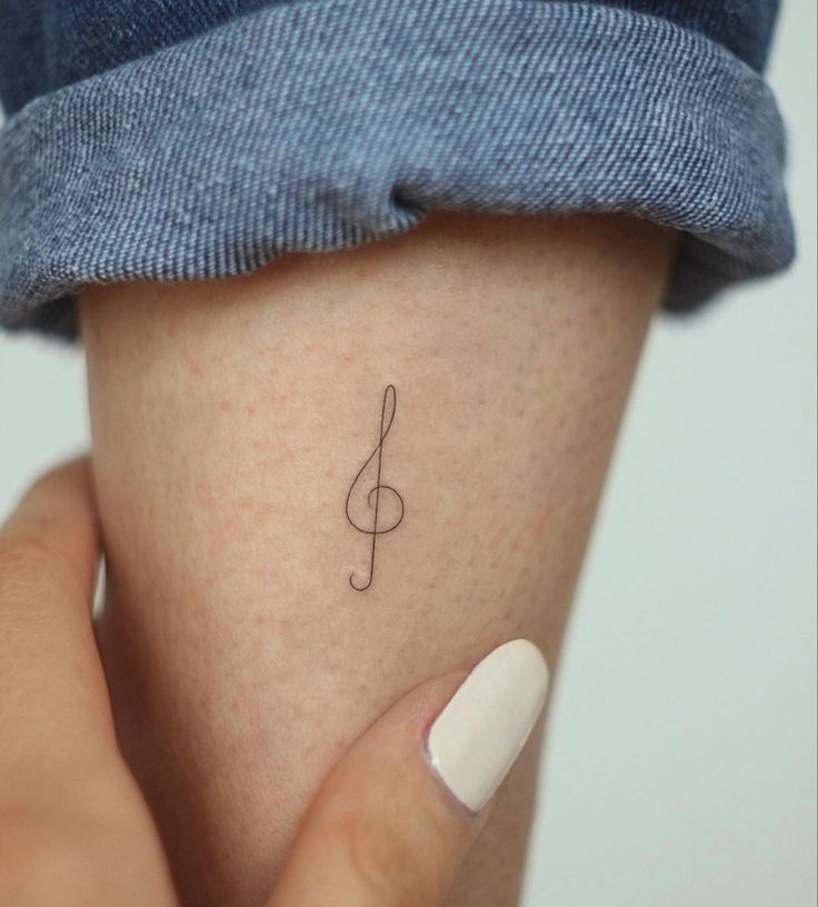 a woman's hand with a small tattoo on her left arm and the word music written in cursive writing