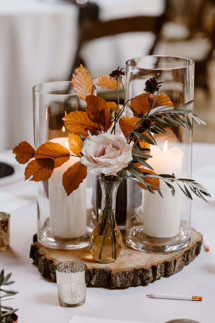 two vases with flowers and candles are on a wood slice at the head table