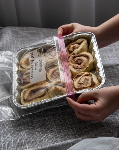 a person holding a tin foil container filled with cinnamon rolls