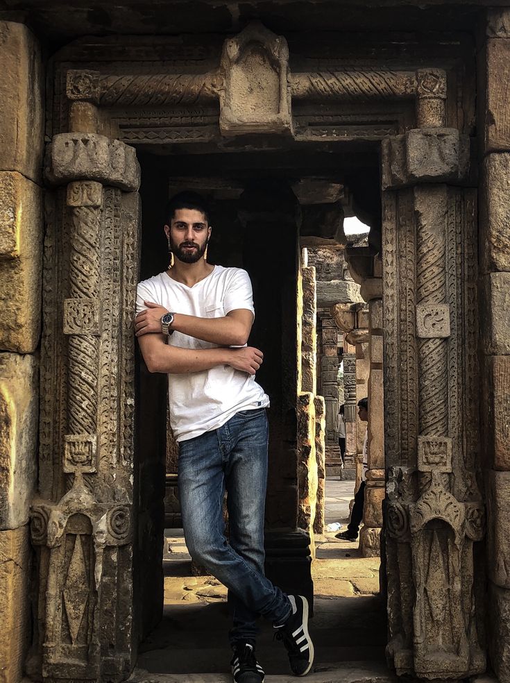 a man in white shirt and jeans standing at entrance to an ancient building with carved pillars