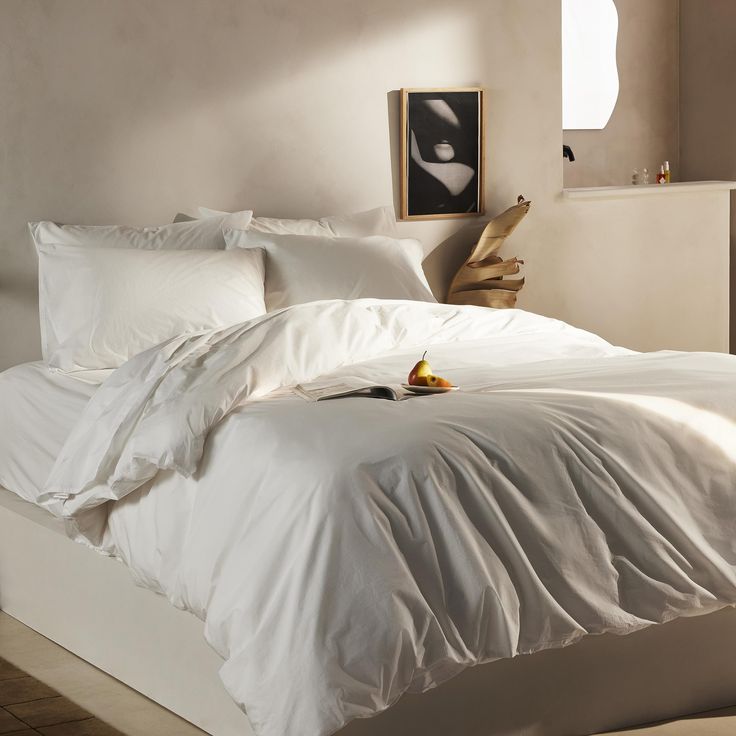 a bed with white sheets and pillows in a room next to a painting on the wall