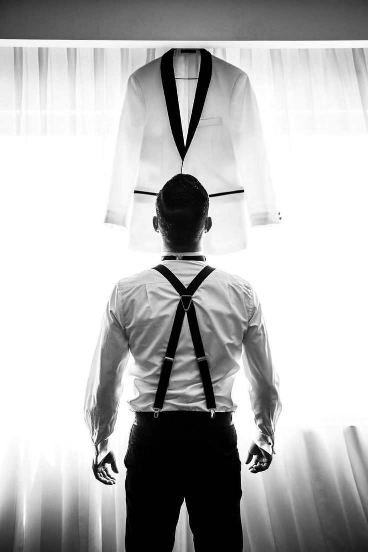 a man standing in front of a window wearing a tie and white shirt with black suspenders