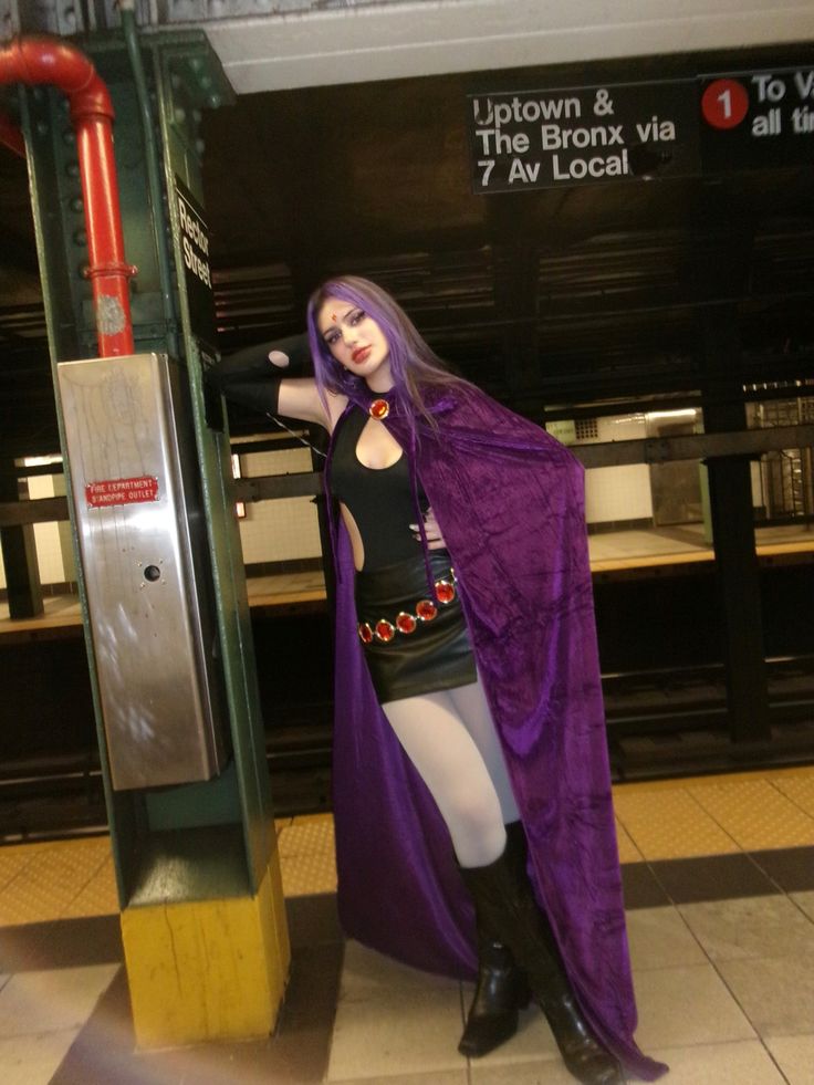 a woman dressed in costume standing next to a train station platform with a purple cape over her shoulders