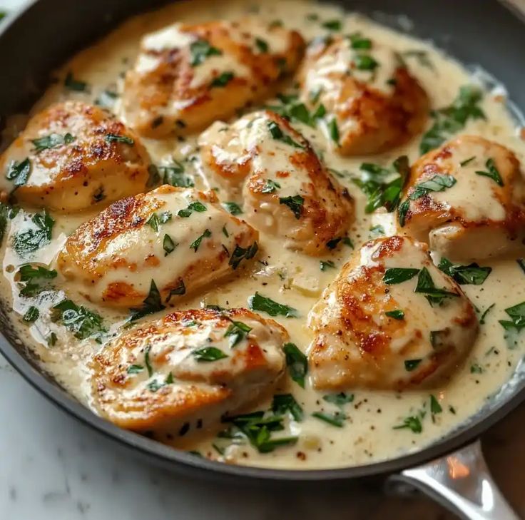 chicken with white sauce and parsley in a skillet on a marble countertop