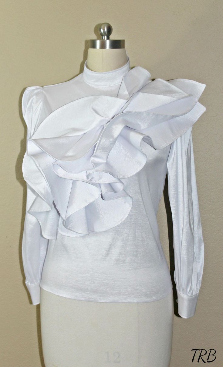 Add a high fashion statement to your wardrobe with this tiered asymmetrical ruffled Blouse. If you love being unique and the center of attention, this blouse will defiantly have all eyes on you! The low cut turtleneck neckline adds a soft, feminine touch and others will defiantly be impressed with your fashion sense. The cascade of asymmetrical ruffles across the front gives the blouse a unique wow factor. The blouse has a tailor fit and is very comfortable to wear. Made of 100% Taffeta, light w Elegant High Neck Top With Ruffles, Elegant High Neck Ruffle Top, Elegant Stretch Tops With Ruffled Collar, Feminine Fitted Top With Ruffles, Elegant Stretch Top With Ruffled Collar, Fitted High Neck Blouse For Party, High Neck Fitted Blouse For Party, High Neck Fitted Party Blouse, Chic Fitted Blouse With Ruffles