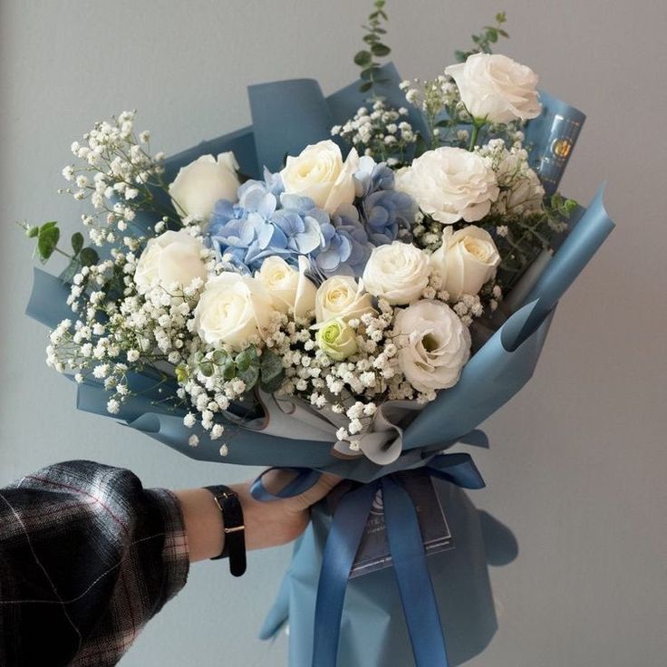 a bouquet of white and blue flowers is being held by a person's hand