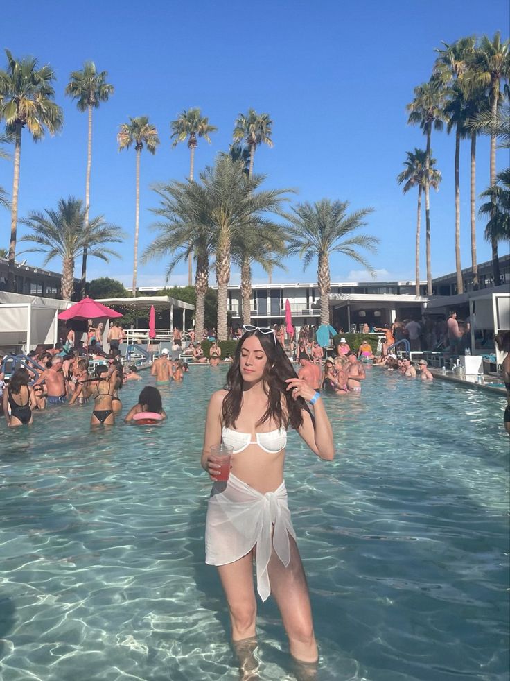 a woman standing in the middle of a pool surrounded by palm trees and other people