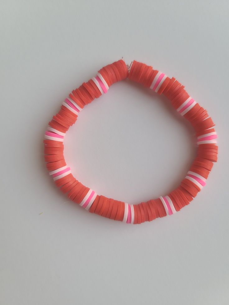 an orange bracelet with pink and white strips on the end is shown against a gray background