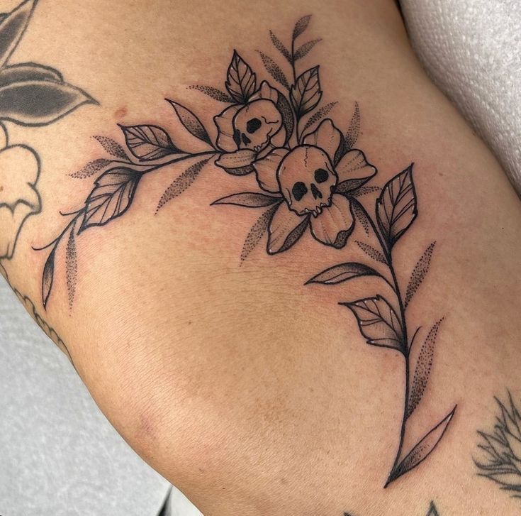 a woman's thigh with flowers and skulls on the side, as well as an arrow