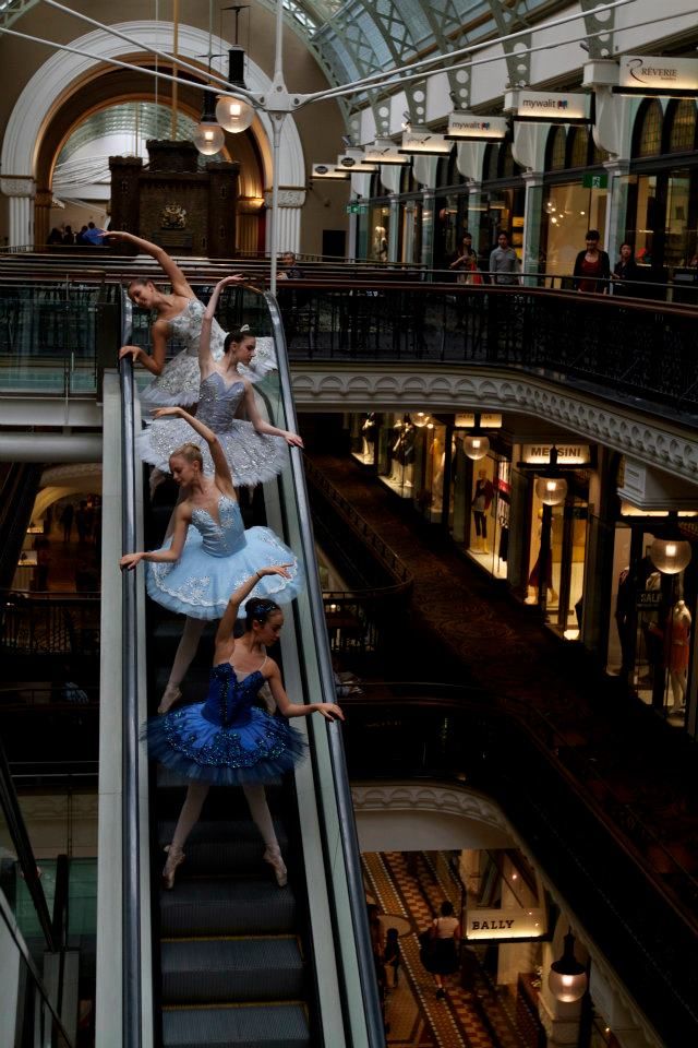 three ballerinas are riding down an escalator in a shopping mall while wearing tutus