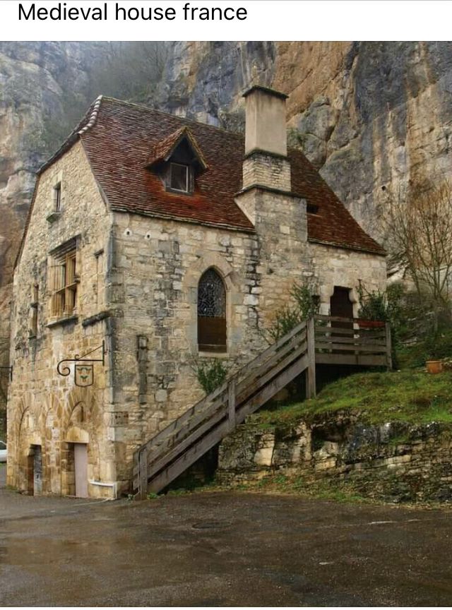 an old stone building with stairs leading up to the front door and side entrance, in front of a mountain range