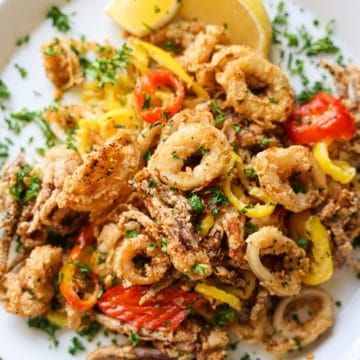 a white plate topped with pasta covered in meat and veggies next to a lemon wedge