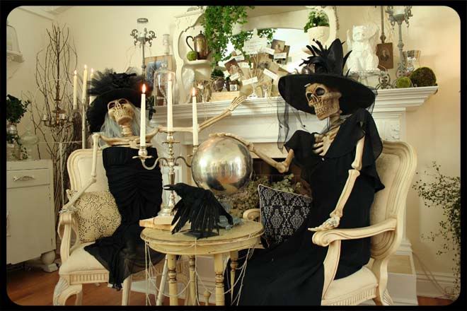 two skeletons dressed in black sitting next to each other near a table with candles on it