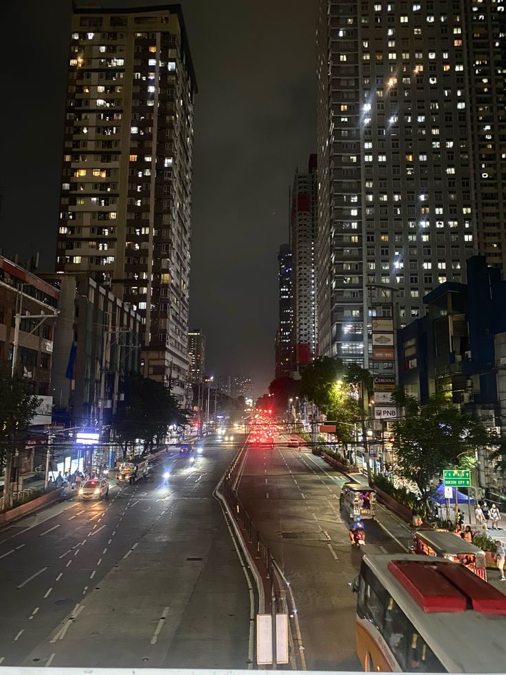 an empty city street at night with tall buildings in the back ground and cars on the road