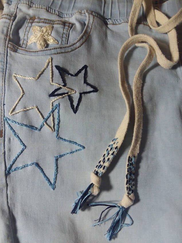 a pair of blue jeans with embroidered stars on the side and tassels attached to them