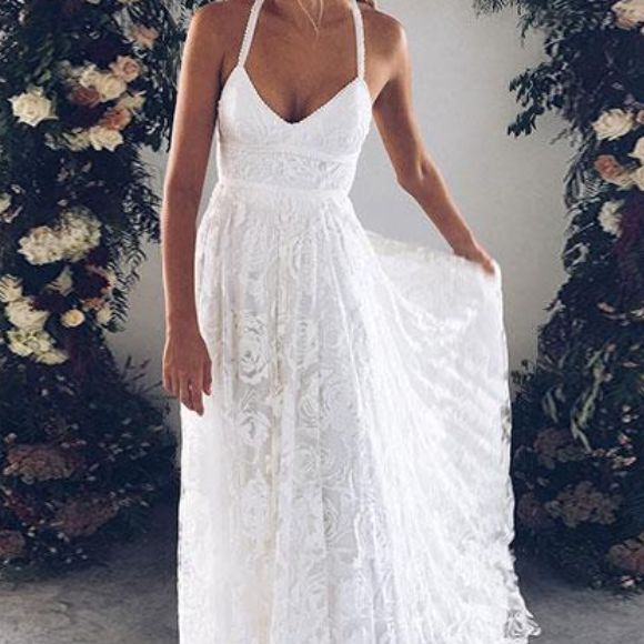 a woman standing in front of a floral arch wearing a white dress with spaghetti straps