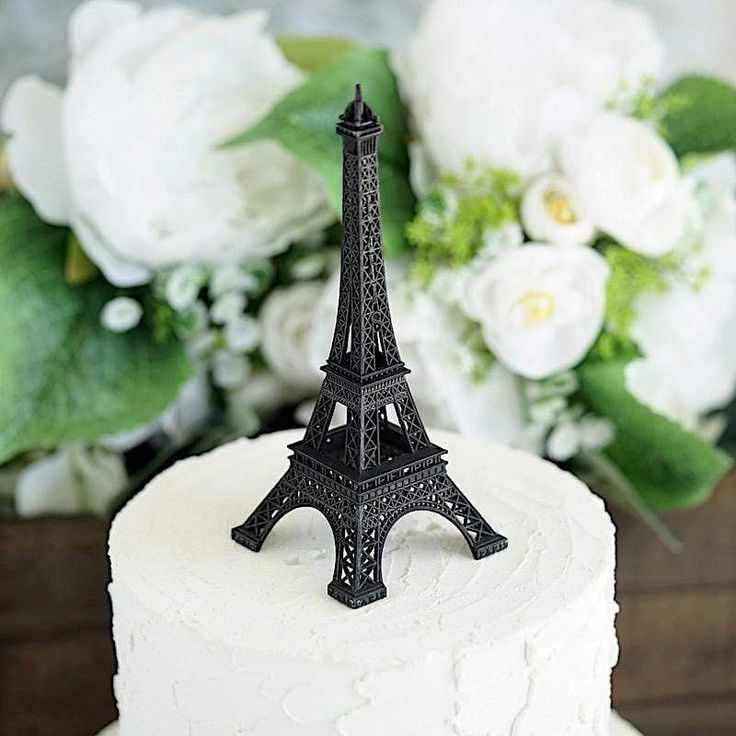 a white cake with a black eiffel tower on top and flowers in the background