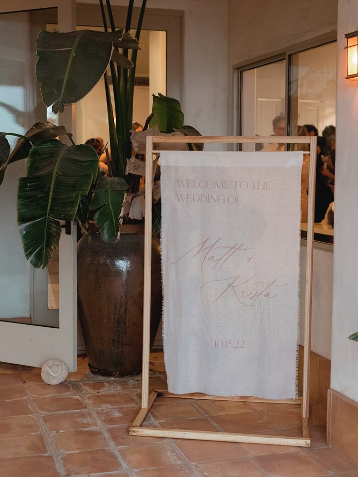 a welcome sign in front of a large potted plant and door to the reception room