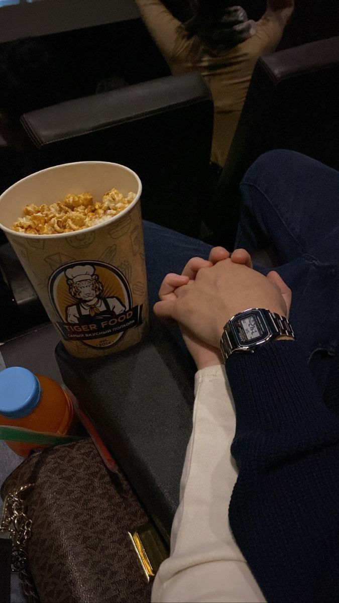 a person sitting on a couch holding their hand over a cup of popcorn