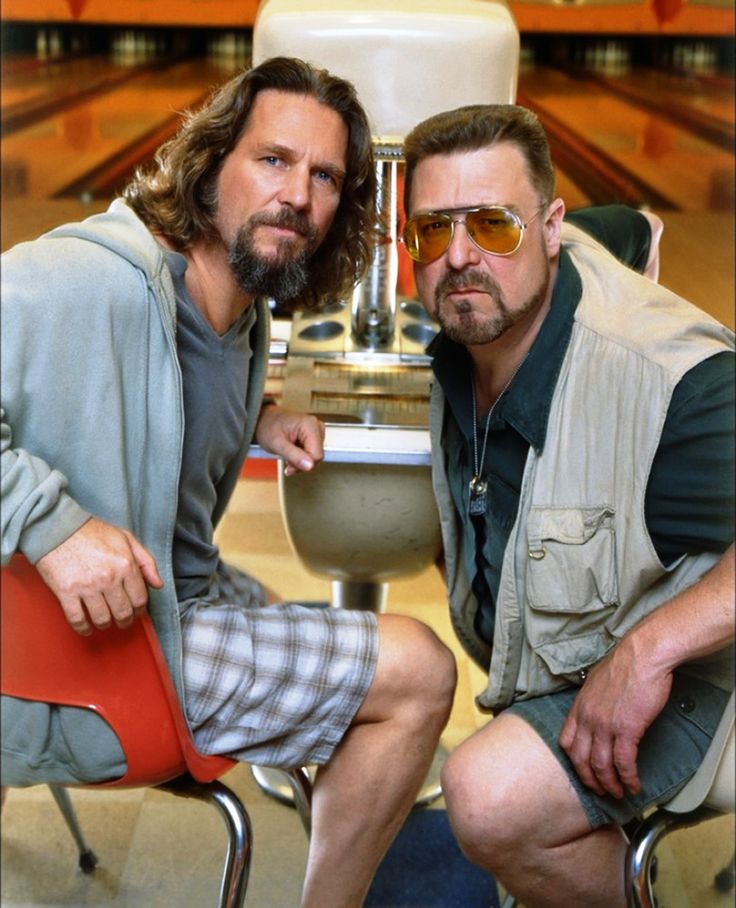 two men are sitting on chairs in front of a bowling ball machine and one has his arm around the chair