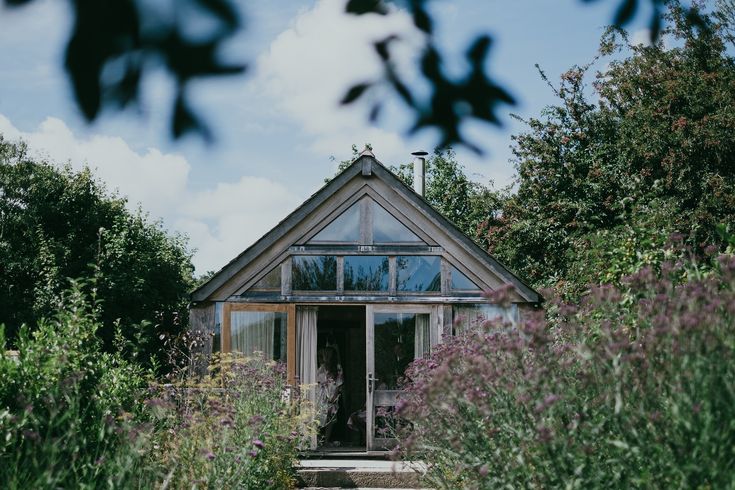 a house sitting in the middle of a lush green field next to trees and bushes