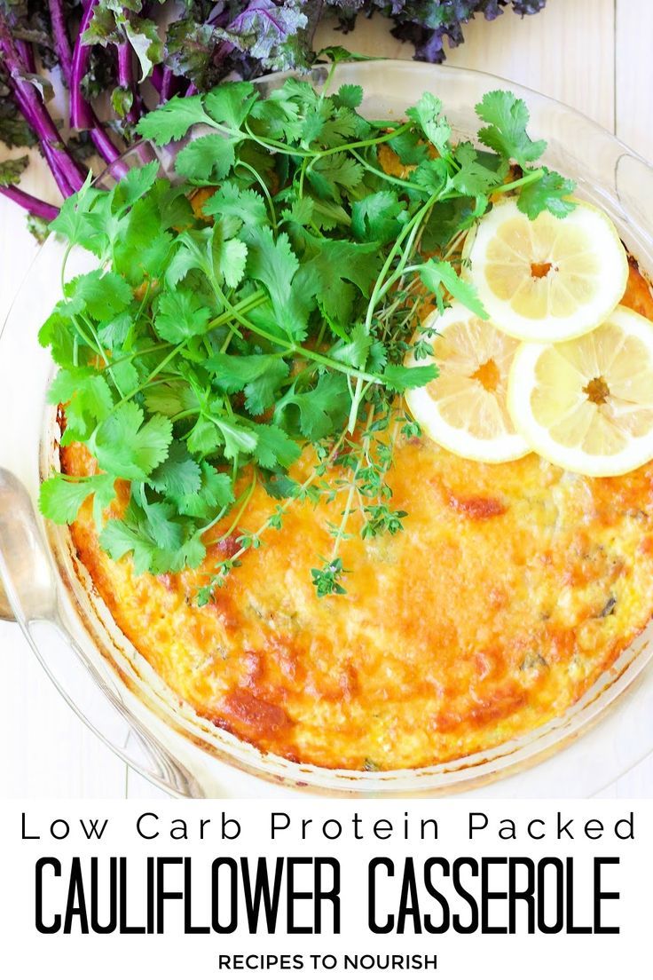 Photo of an overhead view of a round glass casserole dish filled with an egg casserole topped with lots of fresh cilantro and thyme and 3 lemon slices, with a silver serving spoon sitting next to it and fresh purple kale in the background with text that says Low Carb Protein Packed Cauliflower Casserole.