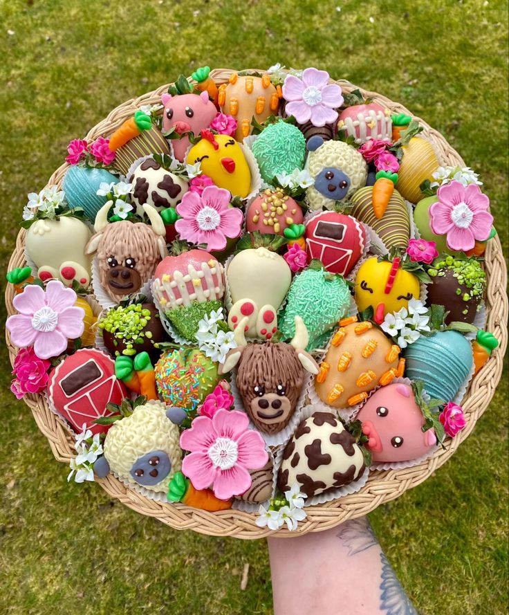 a person holding a basket filled with lots of different types of decorated cookies on top of green grass