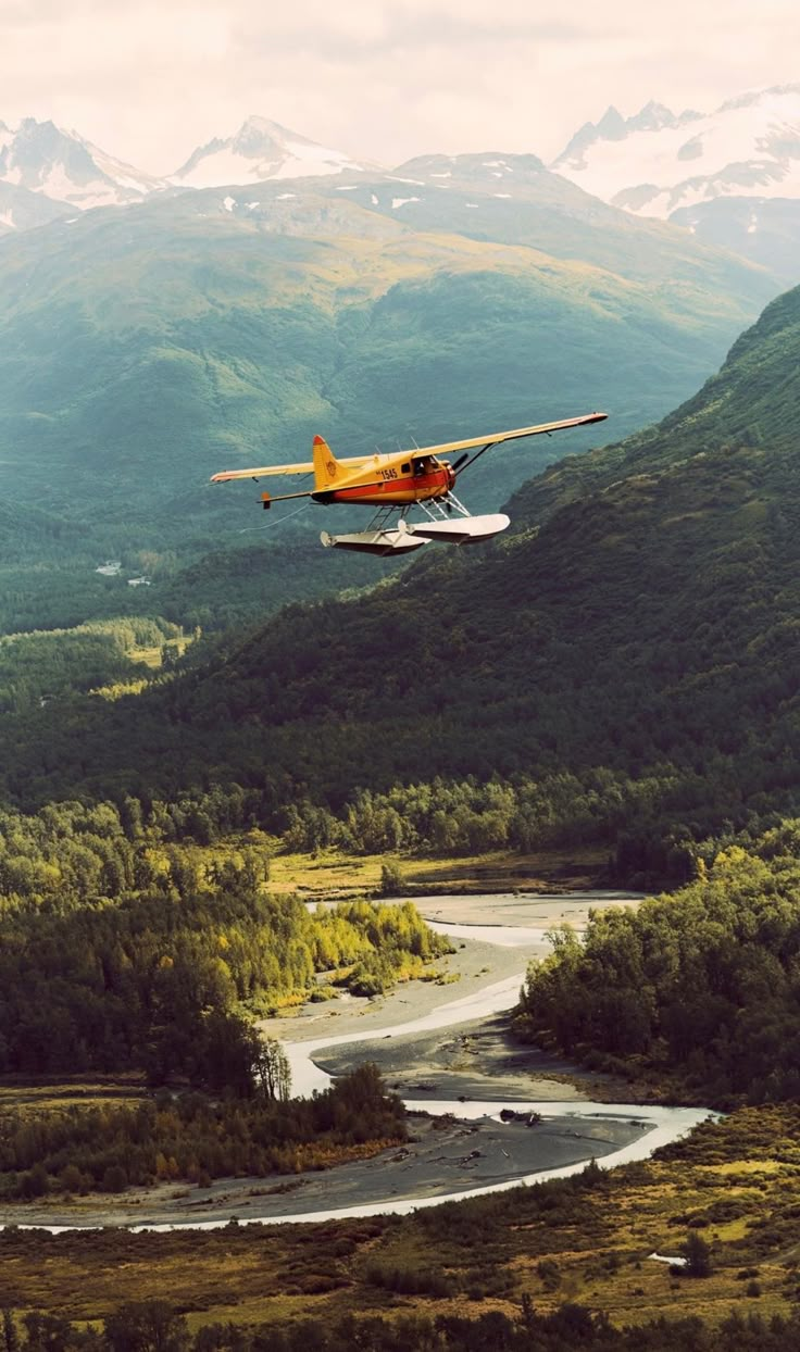 an airplane flying over a river in the mountains