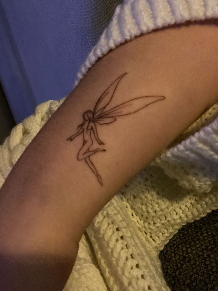 a woman's arm with a tattoo on it that has a small tinkerbell