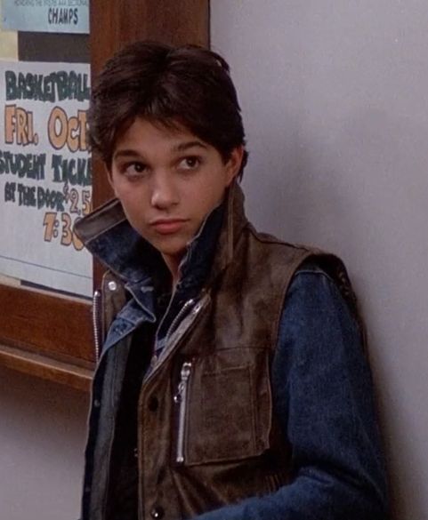 a young boy standing in front of a mirror wearing a leather jacket and jeans, looking at the camera