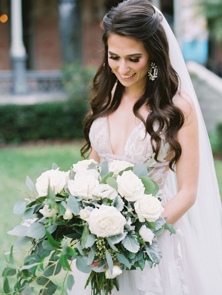 a bride holding a bouquet of flowers in her hand and looking at the camera while standing outside