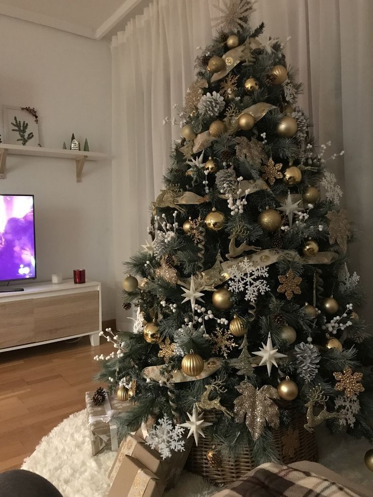 a christmas tree with gold and silver ornaments in front of a flat - screen tv