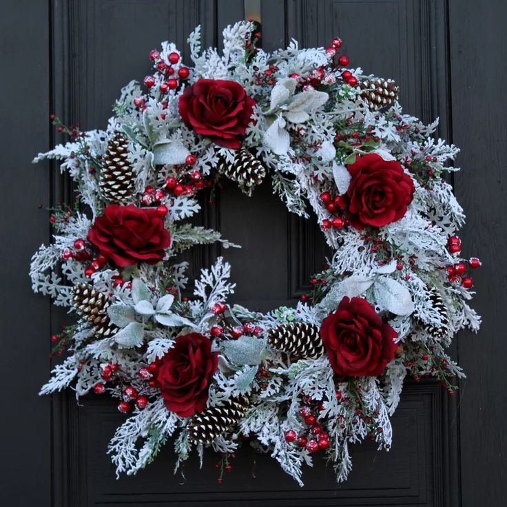 a christmas wreath with red roses and pine cones on a black front door decorated for the holiday season