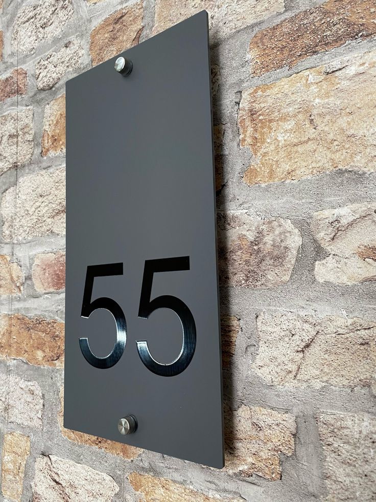 a metal sign with the number 55 on it next to a brick wall in front of a stone wall