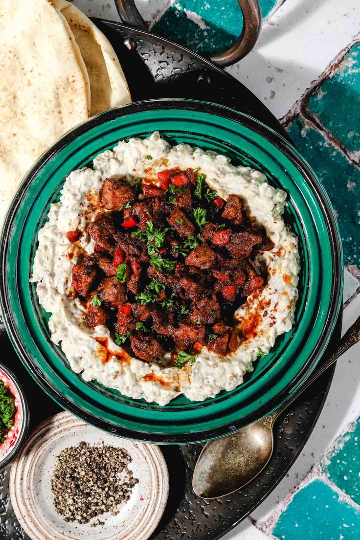 a bowl filled with rice and meat on top of a table next to pita bread