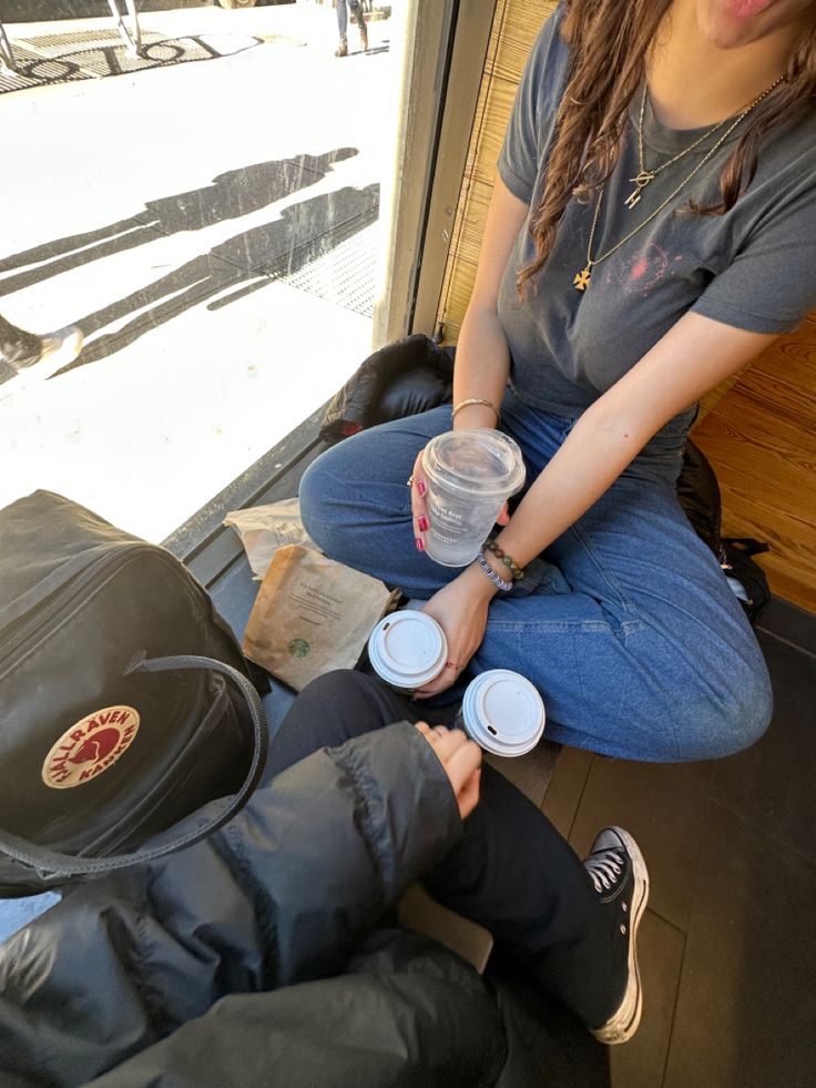 two people sitting on the floor with their hands in each other's pockets and holding coffee cups