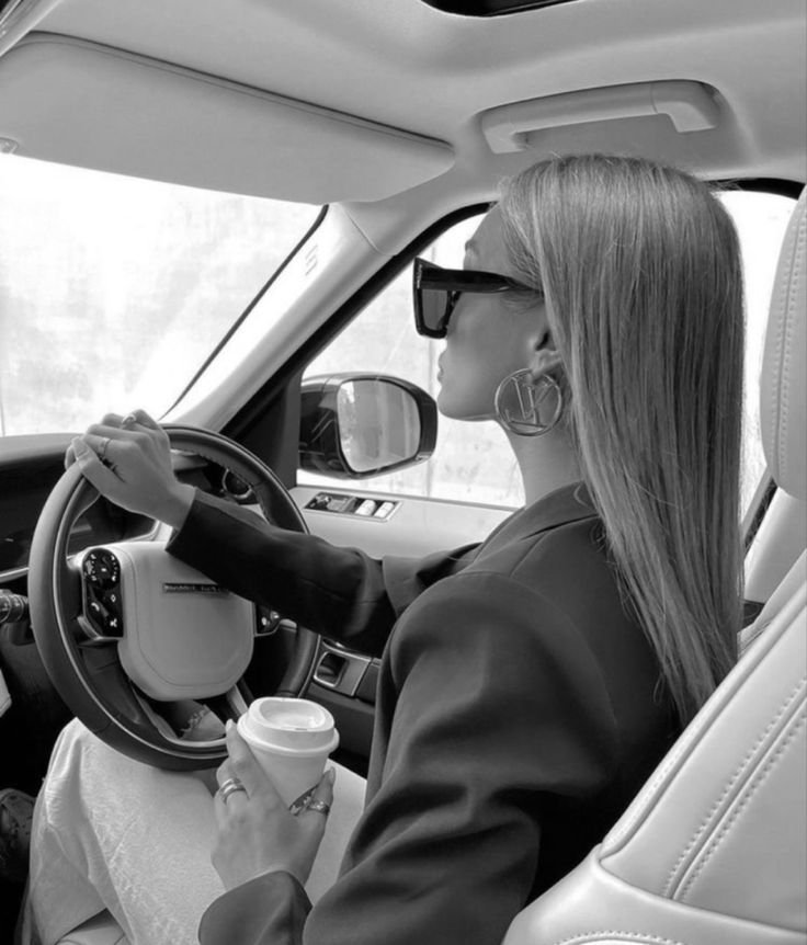 a woman sitting in the driver's seat of a car holding a coffee cup