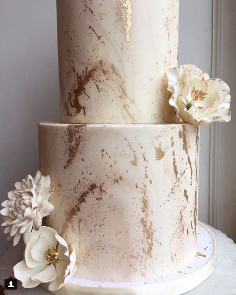 a three tiered cake with white flowers on the top and gold leaf decorations around it