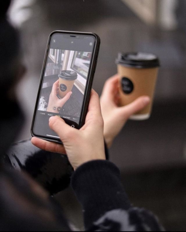 someone taking a photo with their cell phone while holding a cup of coffee in front of them