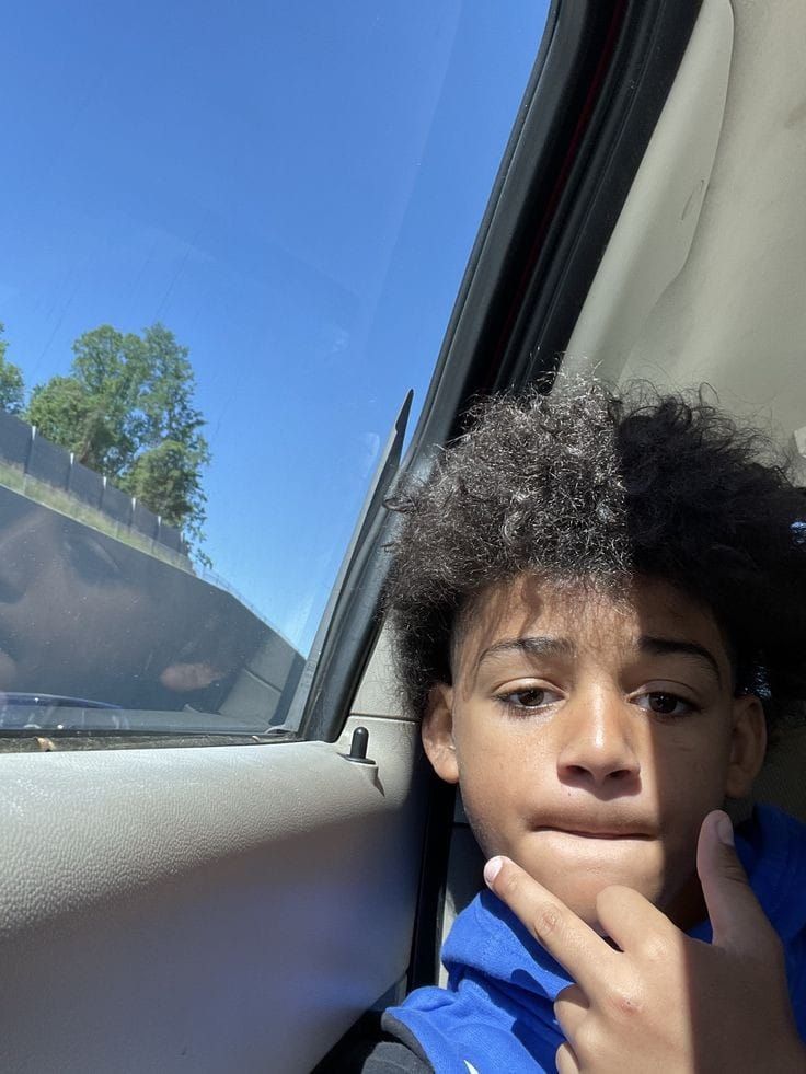 a young boy sitting in the passenger seat of a car with his hand on his chin