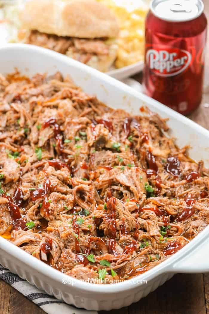 a casserole dish filled with pulled pork and barbecue sauce next to a can of soda